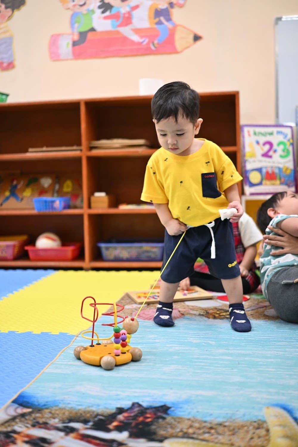 A boy playing with a bead maze toy on the classroom mat