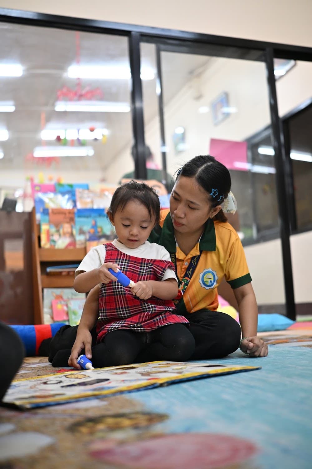 A teacher helping two toddlers with a hands-on activity on the reading mat
