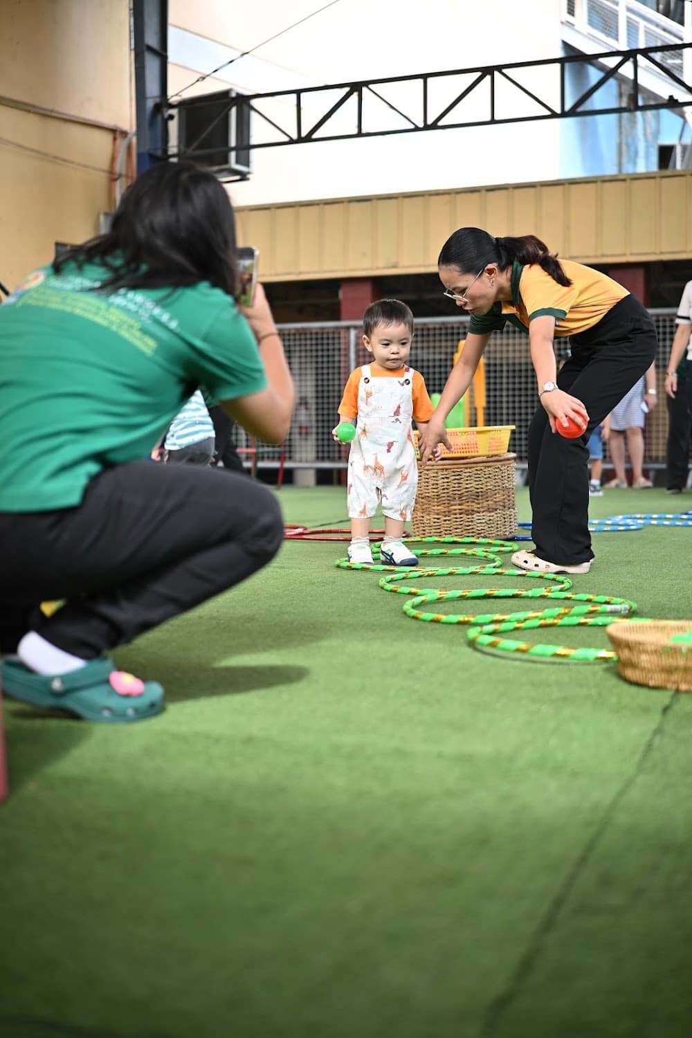 A teacher taking a photo of a toddler on the outdoor play turf