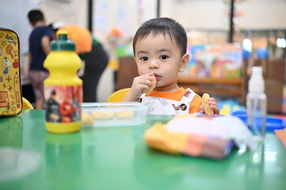 Close-up of a baby in a bib sitting on the classroom mat
