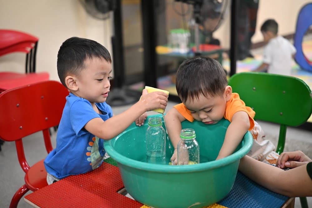 A boy smiling inside a play tunnel holding a sensory bottle